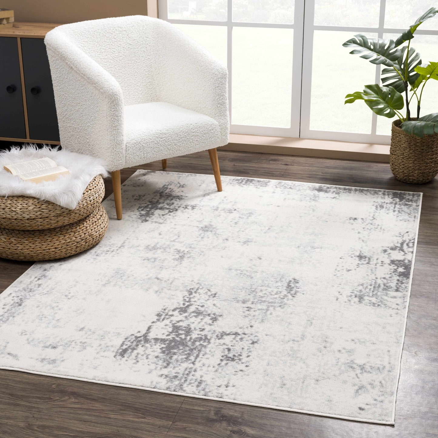 White armchair on a gray area rug in a room with a plant and window.
