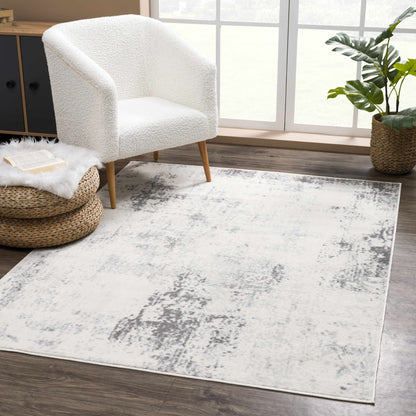 White armchair on a gray area rug in a room with a plant and window.