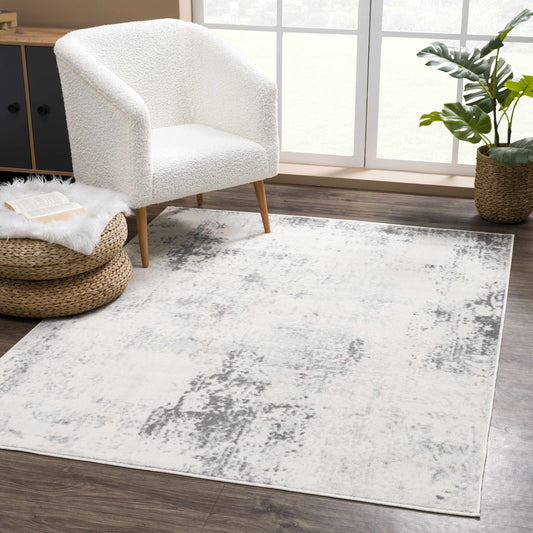 White armchair on a gray area rug in a room with a plant and window.