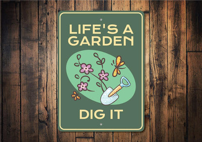 Decorative sign with 'Life's a Garden, Dig It' text and gardening illustrations on a wooden background.