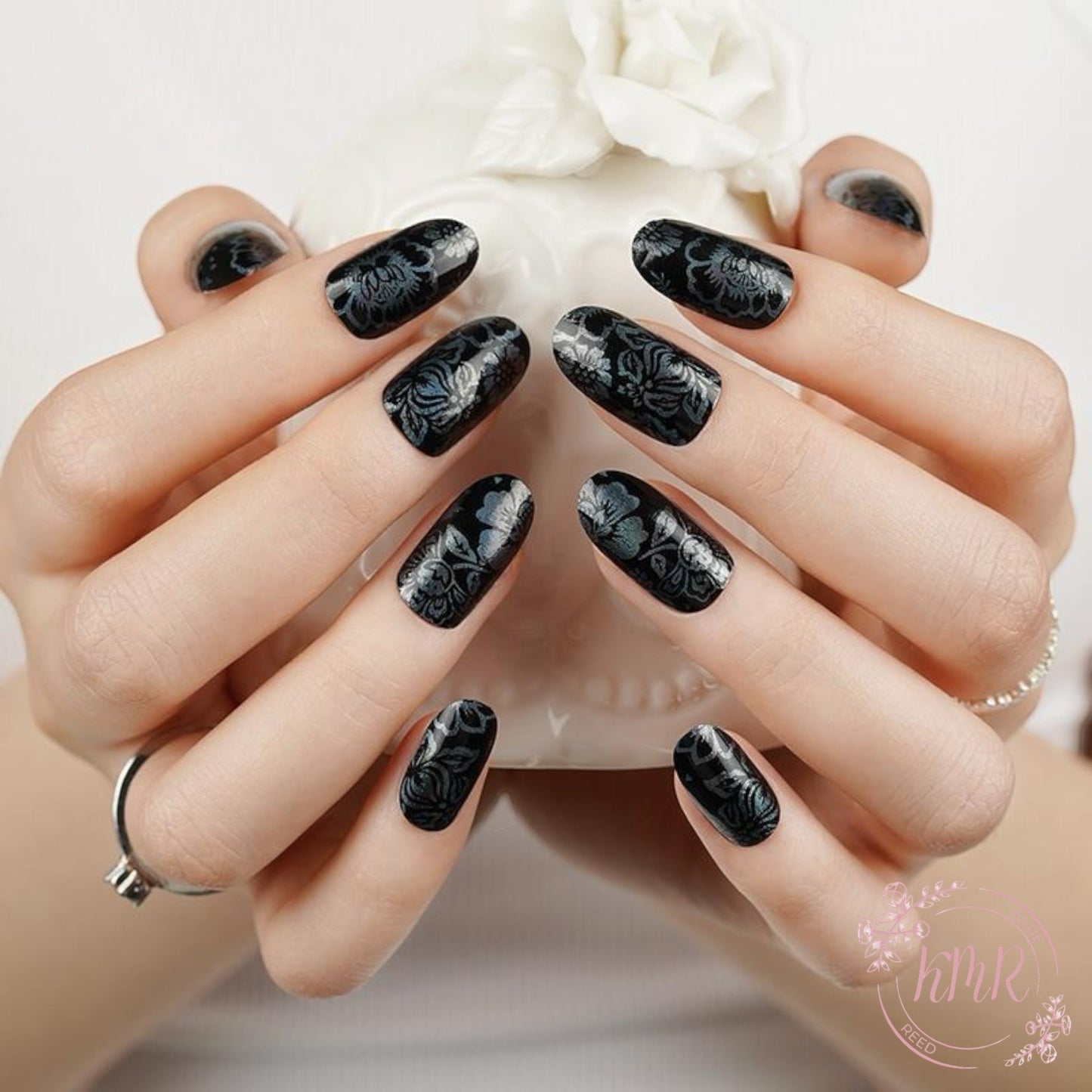 Hand with black floral nail design holding a white flower.