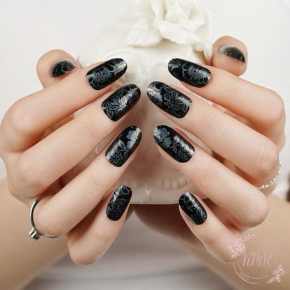 Hand with black floral nail design holding a white flower.