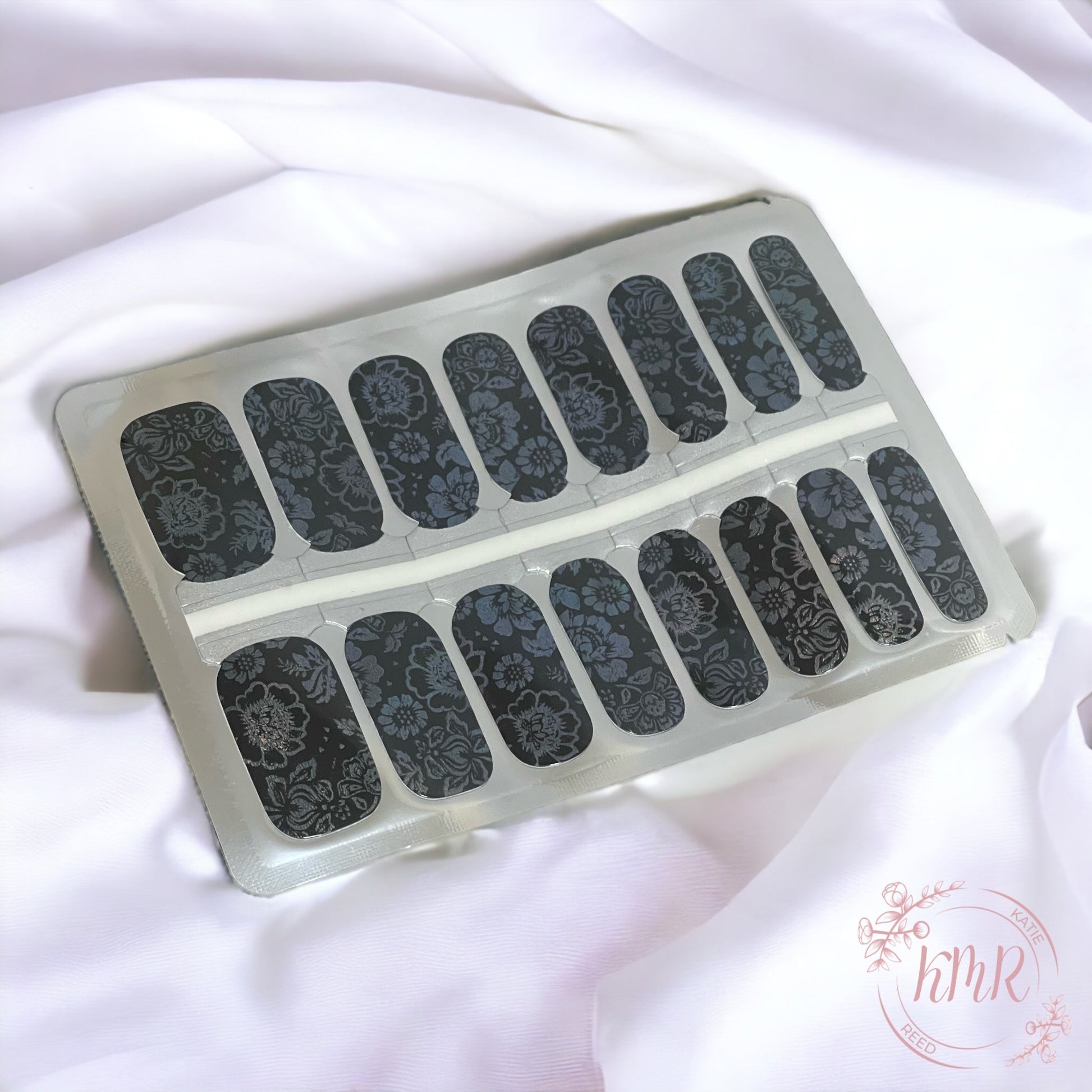 Set of black floral nail art stickers in a clear plastic case on a white fabric background