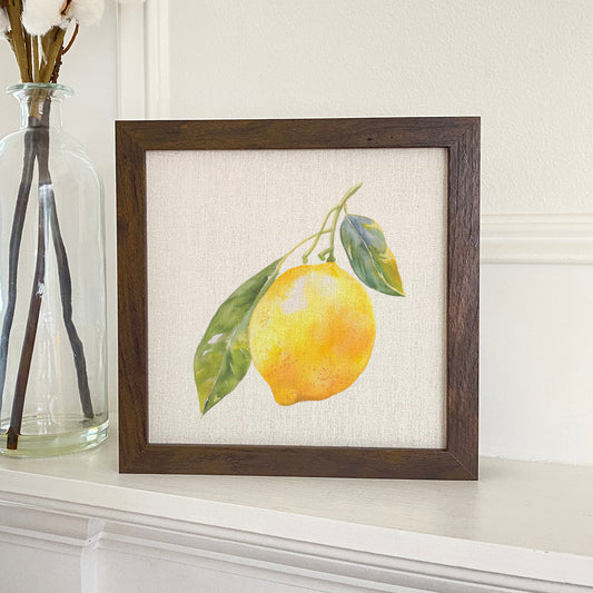 Framed artwork of a lemon with leaves on a white surface.
