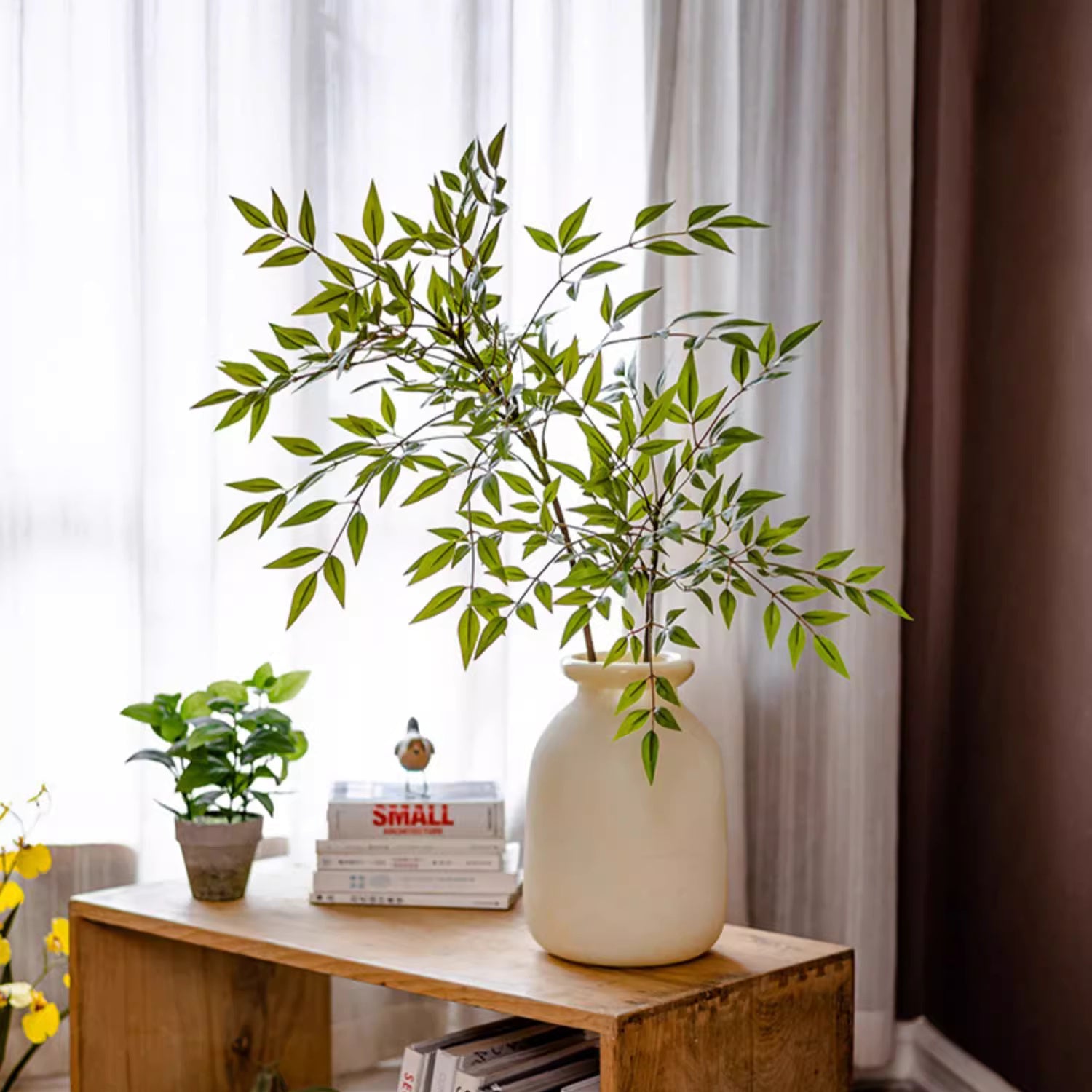 Vase with green leaves on a wooden table against a white curtain background