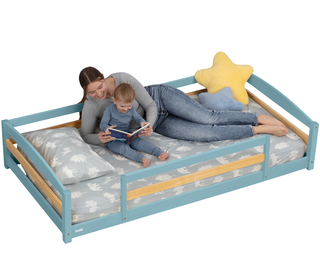 Woman and child lying on a blue children's bed with wooden accents, reading a book.