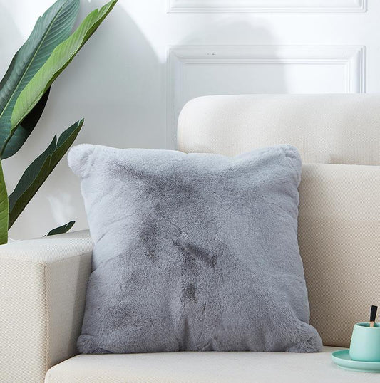 Gray pillow on a beige sofa with a plant and small table in the background
