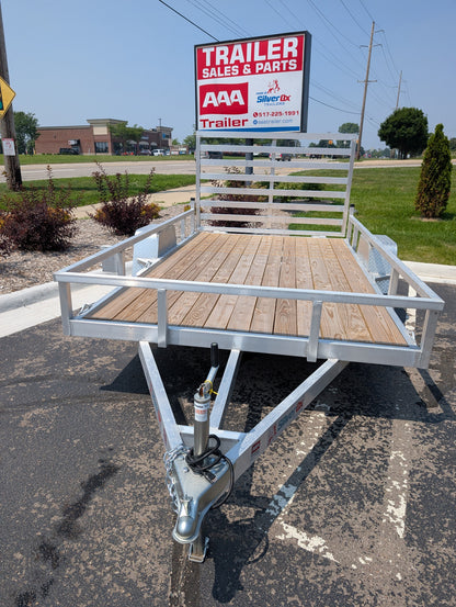 Small utility trailer with wooden floor on a paved surface, with a 'Trailer Sales & Parts' sign in the background.