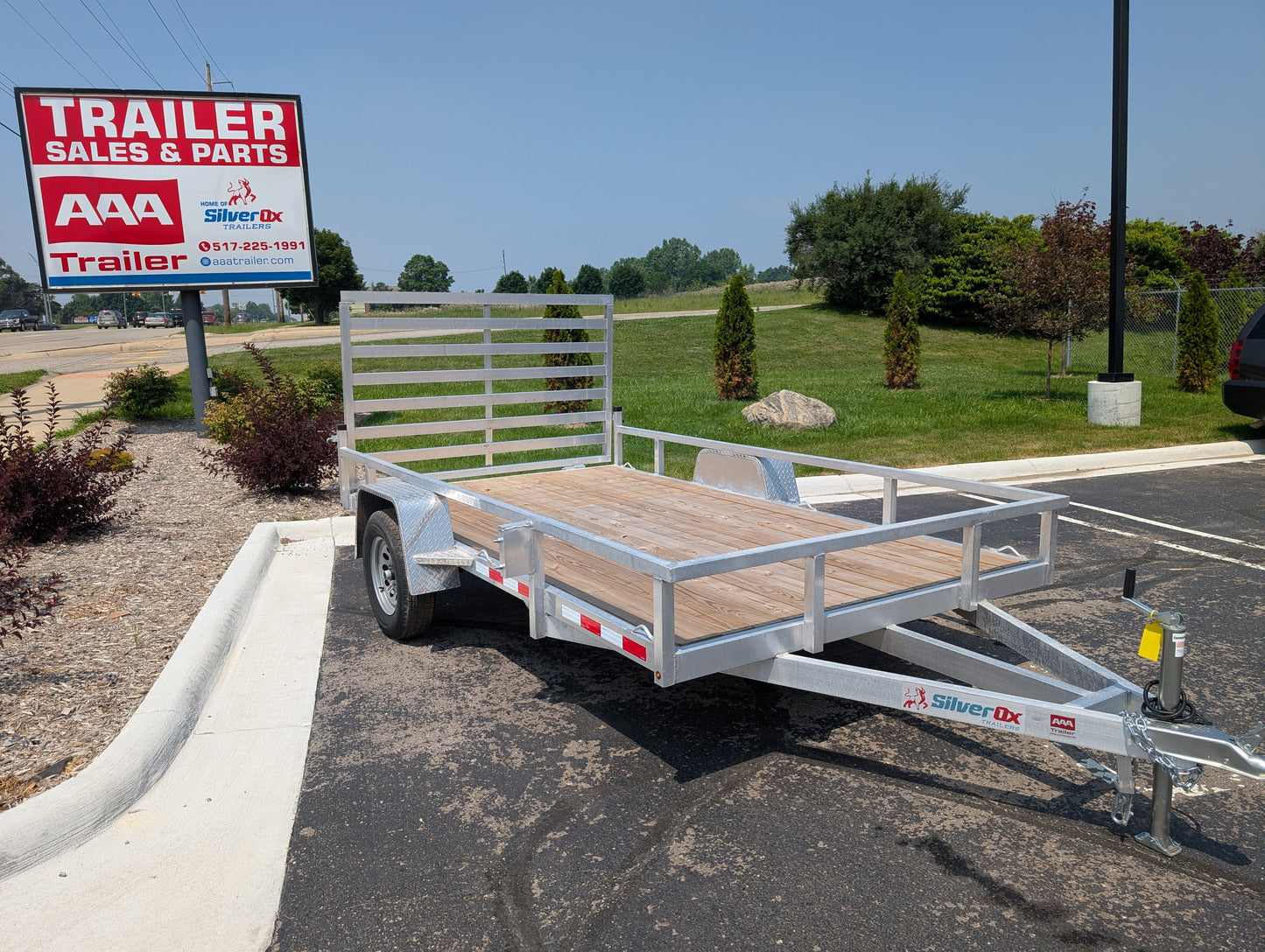 Metal utility trailer parked in a lot with a 'Trailer Sales & Parts' sign in the background.