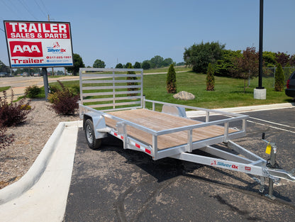 Metal utility trailer parked in a lot with a 'Trailer Sales & Parts' sign in the background.