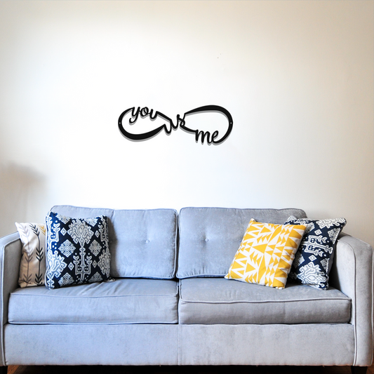 Gray sofa with decorative pillows and a 'you & me' wall decal on a white wall.
