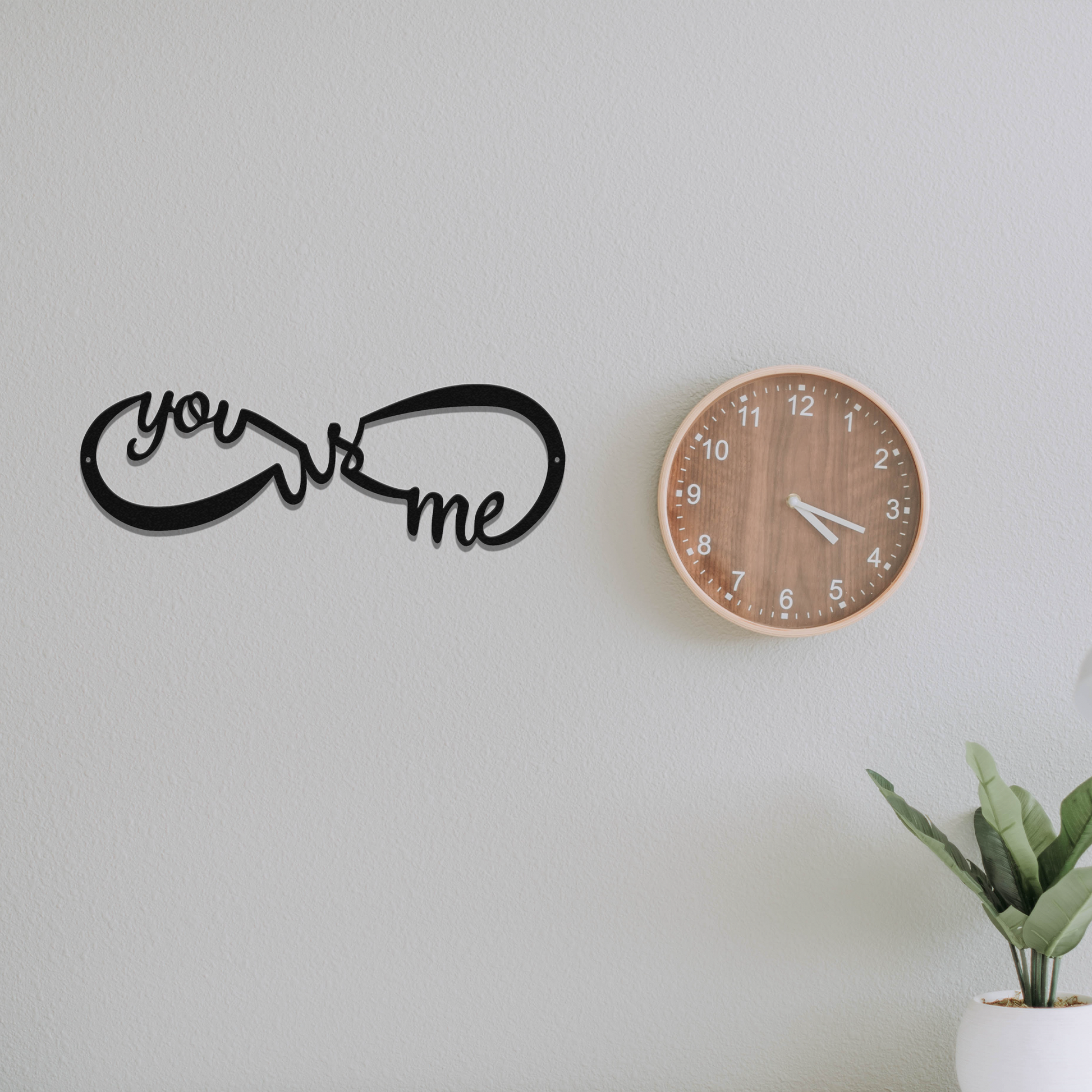 Decorative wall clock with 'you & me' sign on a plain wall.
