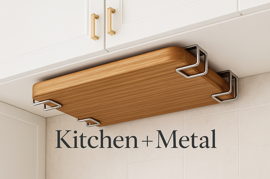 A professional marketing image showing an elegant under-cabinet wooden cutting board with metal brackets mounted beneath white kitchen cabinets. The Kitchen + Metal logo appears in an elegant modern font, creating a sophisticated look that highlights the blend of natural wood and metal elements that define your brand's aesthetic.