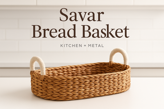 A professional product image of the Savar Bread Basket with white handles, featuring Kitchen + Metal branding in the background