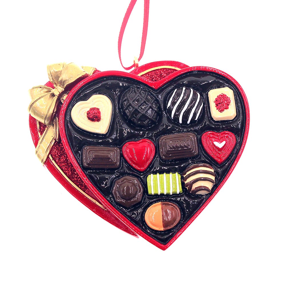 Heart-shaped chocolate box with various chocolates and a gold bow on a white background
