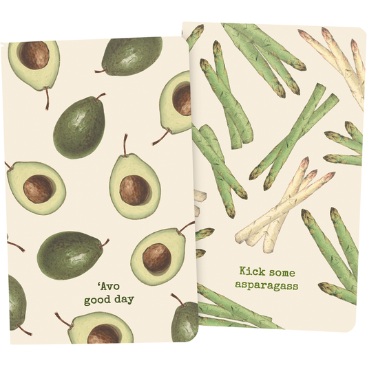 Two large notebooks with vintage-inspired illustrations, one featuring avocado slices and the other with asparagus, and punny titles 'Avo Good Day' and 'Kick Some Asparagass'.