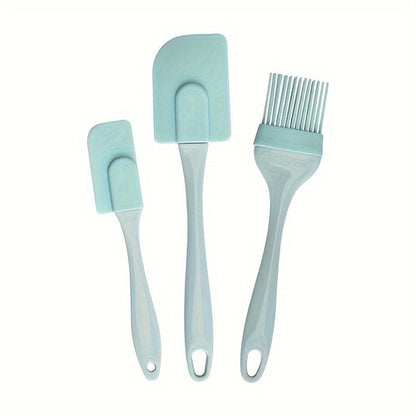 A set of three silicone kitchen utensils, including a spatula, a brush, and a scraper, in a light blue color, displayed on a two-tone background with orange and blue sections.