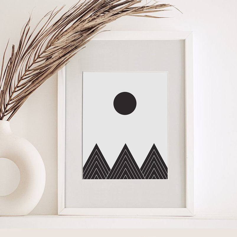 Framed black and white abstract art print with mountains and a sun on a white surface.