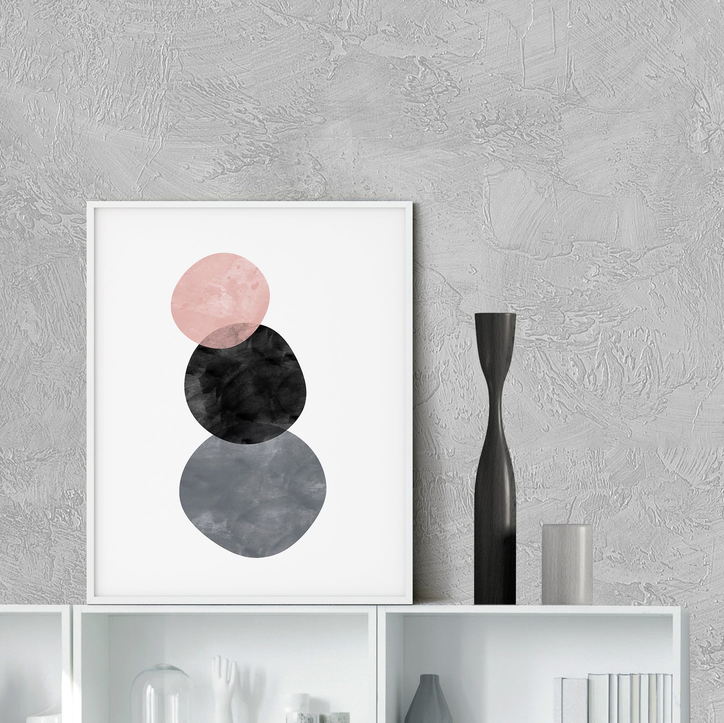Framed abstract art print with pink, black, and gray circles on a textured wall.