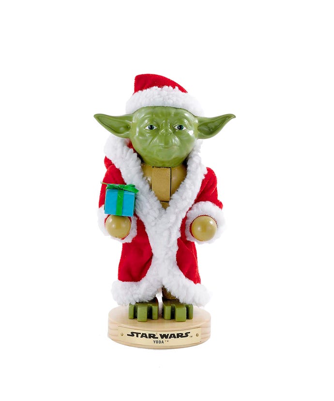 Yoda figurine in a Santa outfit holding a gift on a white background