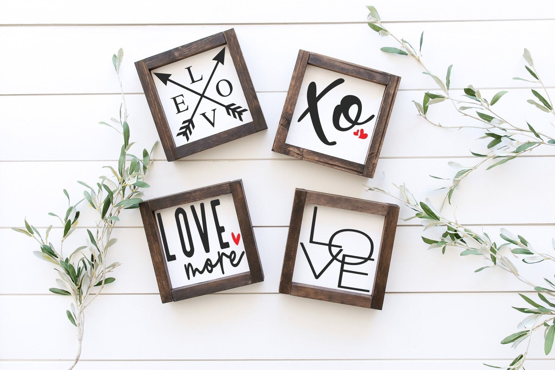 Four wooden frames with 'LOVE' and heart designs on a white wooden surface with greenery.