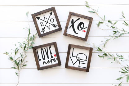 Four wooden frames with 'LOVE' and heart designs on a white wooden surface with greenery.
