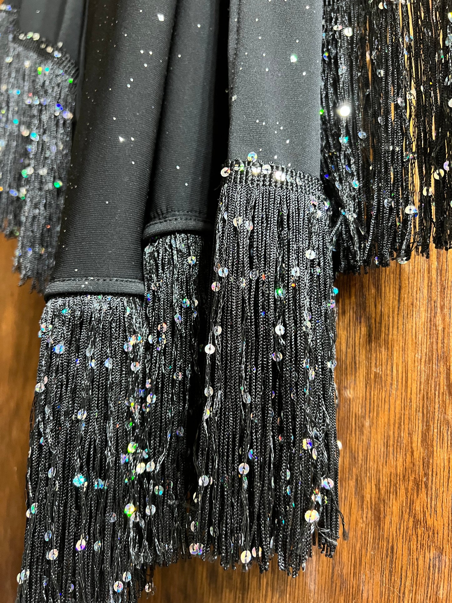 Black sequin dress with fringe details on a wooden surface