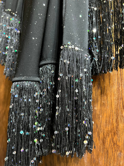 Black sequin dress with fringe details on a wooden surface