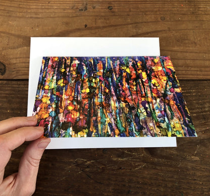 Colorful abstract painting on a white card held by a hand on a wooden surface