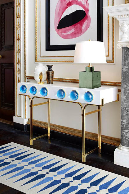 Decorative console table with blue spherical objects, a lamp, and framed artwork in a stylish interior setting.