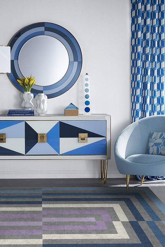 Modern interior with a geometric-patterned dresser, round mirror, and blue chair.