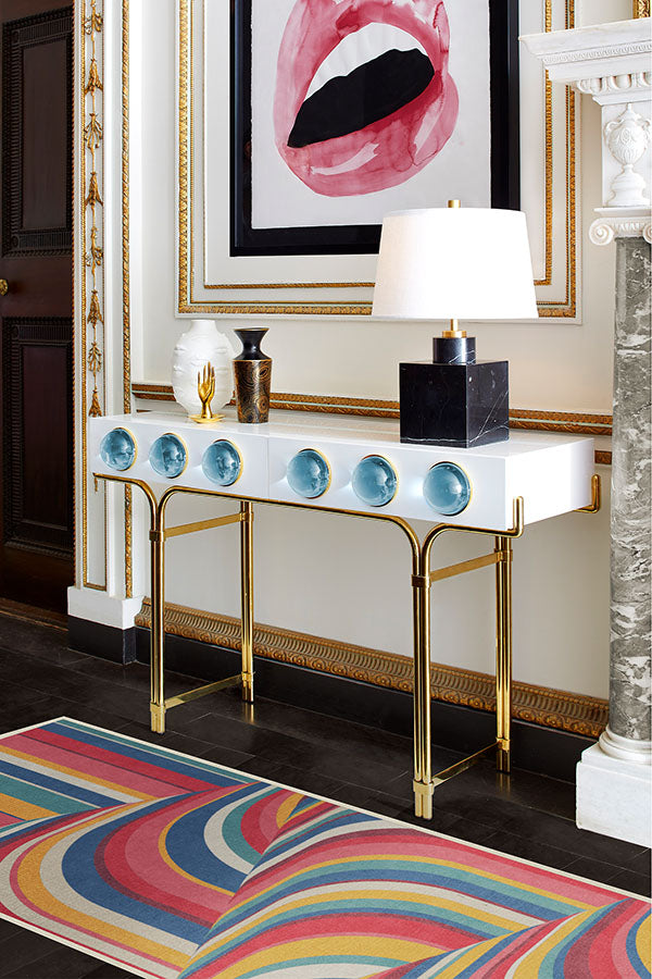 Decorative console table with blue spherical objects, gold legs, and a colorful rug on a dark wooden floor.