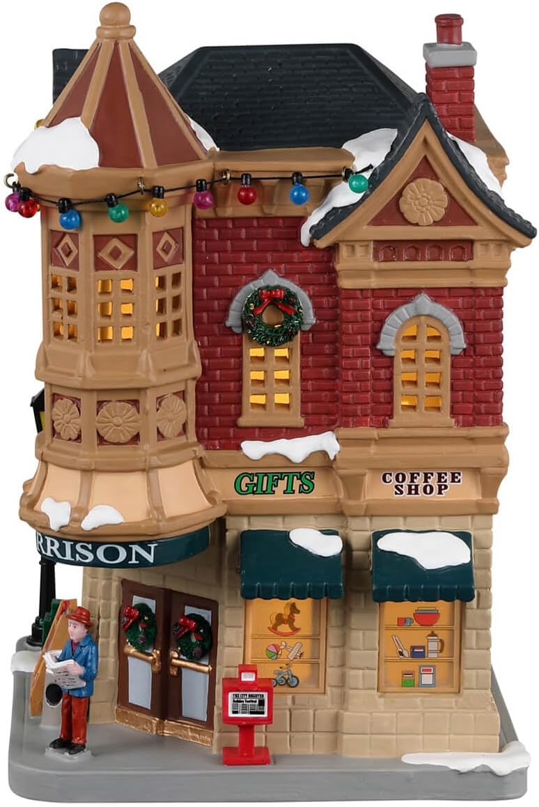 Decorative model of a snowy village street with shops and a person reading a newspaper.